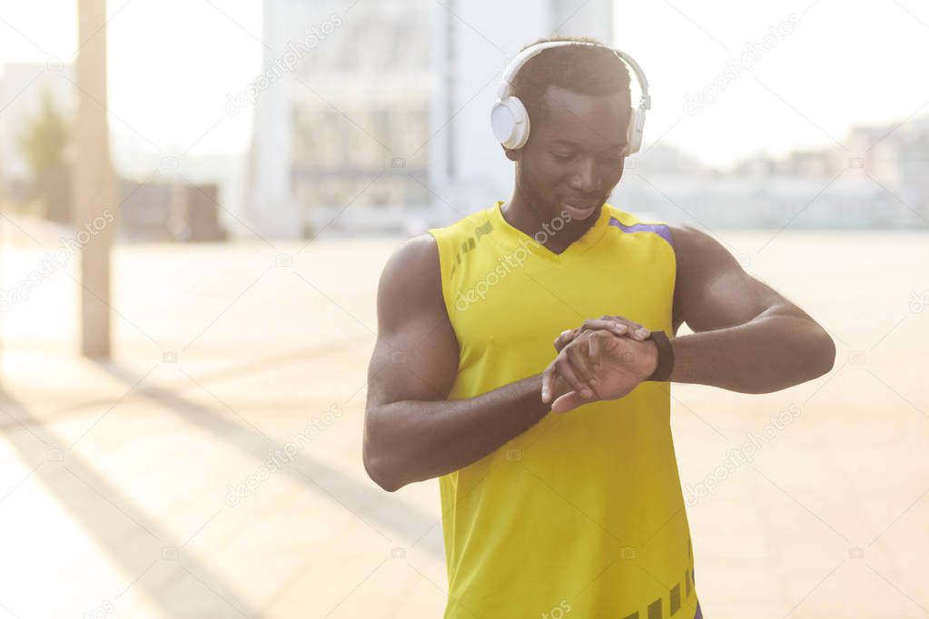 african american man with perfect body looking at at smartwatch on hand and counting burned calories after jogging 