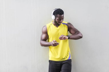 Afro-Amerikan sportif adam akıllı telefon tutarak ve smartwatch gri arka plan üzerinde seyir
