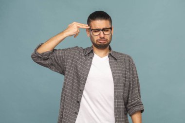 siyah gözlük ve kameraya bakarak ve eli silah tutan mavi arka plan üzerinde oturum rahat tarzı kıyafetler komik yakışıklı adam sakallı  