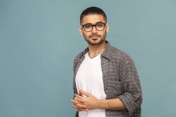 bearded handsome man with black glasses in casual style looking at camera and smiling on blue background