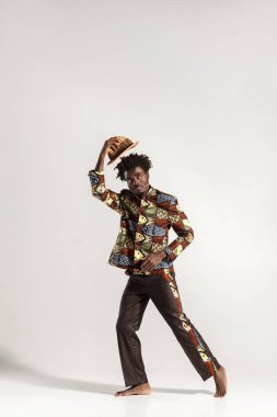 şapka tutan ve gri arka plan üzerinde poz kameraya bakarak Afro-Amerikan yakışıklı