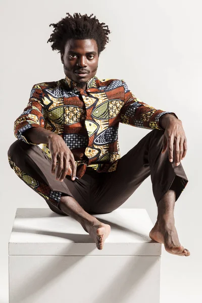 moda Afrika adam beyaz zemin üzerine küp üzerinde oturan izole iken poz yakın çekim 