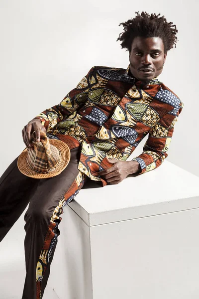  Afrika kökenli Amerikalı manken gri arka plan üzerinde beyaz küp üzerinde eğilerek şapka ile geleneksel giysiler içinde