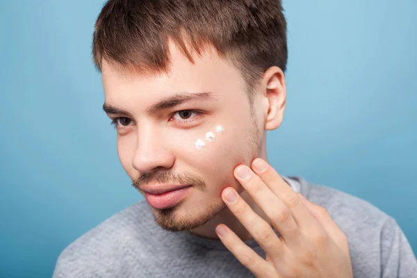 Portrait of young brunette man applying facial cream. indoor stu — Stock Photo, Image