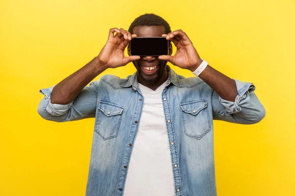 Porträt eines positiven, fröhlichen Mannes, der die Augen mit dem Handy verdeckt — Stockfoto