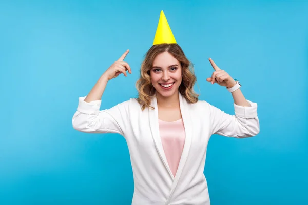 Portrait de jeune femme heureuse avec un cône drôle sur la tête pointant un — Photo