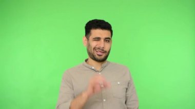 Her şey yolunda. Tişörtlü mutlu esmer adam iyi bir jest yapıyor ve göz kırpıyor, saygı gösteriyor ve onaylıyor, öneriyle tatmin oluyor. Stüdyo içi çekim, yeşil arka plan, krom anahtar.