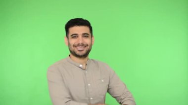 Tişörtlü neşeli esmer adam el ele tutuşuyor ve kameraya gülümsüyor. Onaylayarak başını sallıyor. Kendinden emin ve başarılı görünüyor. Stüdyo içi çekim, yeşil arka plan, krom anahtar.