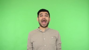 Tişörtünü çıkartıp dilini dışarı çıkaran, iki gözünü kırpan, çocuksu suratını ekşiten, suratını ekşiten, oynaşan komik esmer adam. Stüdyo çekimi, yeşil arkaplan, krom anahtar