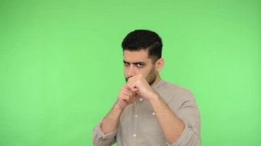 Tişörtünde kılları olan kızgın esmer bir adam, yumruklarını kaldırıyor, kameranın önünde havayı yumrukluyor, suratını asık bir ifadeyle boks yapıyor, kendini savunuyor. Stüdyo içi çekim, yeşil arka plan, krom anahtar.
