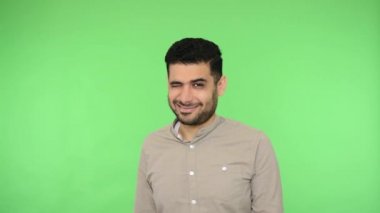 Tişörtlü, neşeli, esmer yakışıklı, şakacı, flört eden, kameraya gülümseyen, randevuya davet eden bir adam. Bir sır biliyor. Stüdyo içi çekim, yeşil arka plan, krom anahtar.