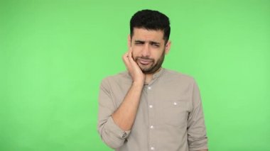 Tişörtlü mutsuz esmer adam, tıraşsız çenesini kaşıyor, fikri düşünüyor, zor soruyu düşünüyor, şüpheleri var, tereddütleri var. Stüdyo içi çekim, yeşil arka plan, krom anahtar.