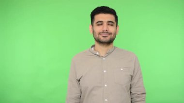 Dikkatli yoga, akıl sağlığı. Barışçıl esmer adam tişörtünün içinde ellerini bağlayıp dua ediyor, gözleri kapalı meditasyon yapıyor, rahatlıyor. Stüdyo içi çekim, yeşil arka plan, krom anahtar.