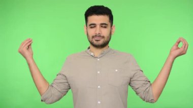 Yogaya özen gösterin. Tişörtünde kılları olan barışçıl esmer adam Mudra hareketi yapıyor ve meditasyon yapıyor, ara veriyor, rahatlıyor ve stresle başa çıkıyor. Stüdyo içi çekim, yeşil arka plan, krom anahtar.
