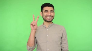 Zafer! Son derece mutlu, tişörtünde iki parmak hareketi ya da barış sembolü olan mutlu ve neşeli bir adam mutluluktan gülümseyip dans ediyor. Stüdyo içi çekim, yeşil arka plan, krom anahtar.