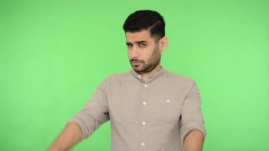 Gömleği tüylü esmer adam çerçeveden parmaklarıyla bakıyor, kameraya odaklanıyor profesyonel fotoğrafçı görünümlü, fotoğraf çekiyor. Stüdyo içi çekim, yeşil arka plan, krom anahtar.