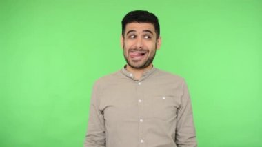 Tişörtünde kıl olan, burnunu karıştıran, sümük çıkaran, dilinden sarkan ve eğlenen komik, pozitif esmer adam. Stüdyo içi çekim yeşil arka plan, krom anahtar