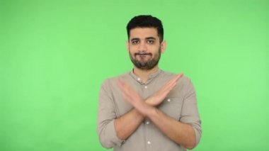 Tişörtünde kılları olan mutsuz esmer adam X işareti işareti hareketi gösteriyor ve kesin hayır diyor. Bu son, yasaktır. Stüdyo içi çekim, yeşil arka plan, krom anahtar.