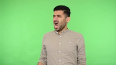 Yorgun, uykulu esmer, gömleği kıllı, ağzı elle esneyen, yorgun ya da kayıtsız görünen uykusuz bir adam. Stüdyo içi çekim, yeşil arka plan, krom anahtar.