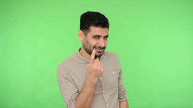 Hey sen, güzellik, bana gel! Tişörtünde tüyleri olan yakışıklı esmer adam çekici gözlerle bakıyor ve yaklaşmak için işaret ediyor, davetkar hareketler yapıyor. Stüdyo içi çekim, yeşil arka plan, krom anahtar.