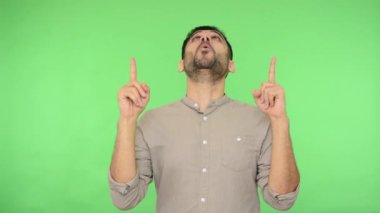 Yukarı bak! Tişörtlü, mutlu, esmer bir adam. Tanıtım metni ya da ürün tanıtımı için reklam alanı gösteriyor. Kopya alanı. Stüdyo içi çekim, yeşil arka plan, krom anahtar.