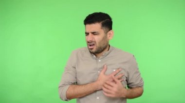 Kalp kırıcı. Gömleği tüylü hasta esmer adam göğsünü sıkıca kavrıyor ve zor nefes alıyor, iyi hissetmiyor, kalp krizi geçiriyor ya da ağrılı kramplar geçiriyor. Stüdyo içi çekim, yeşil arka plan, krom anahtar.