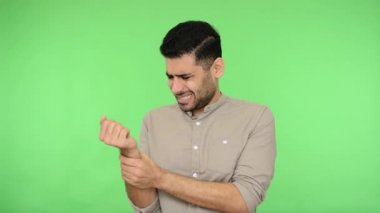 Yaralı el. Tişörtünde tüyleri olan, bileği ağrıyan, eli burkulmuş, eklem iltihabı olan, karpal tünel sendromu olan hasta esmer bir adam. Stüdyo çekimi, yeşil arkaplan, krom anahtar