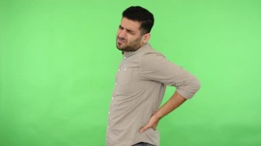 Hasta, yakışıklı, sakallı, bej tişörtlü, yeşil duvarda sırtı ağrıyan genç bir adam.
