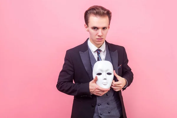Portrait of elegant self-confident man holding white mask, looki