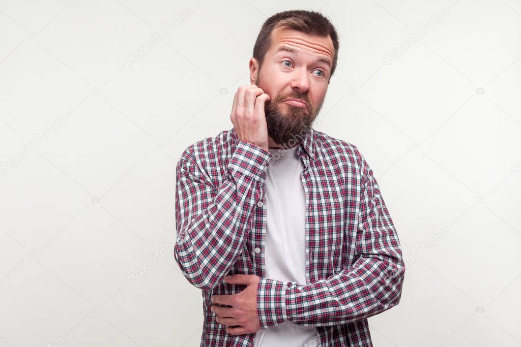 Portrait of thoughtful man in plaid shirt scratching his beard a