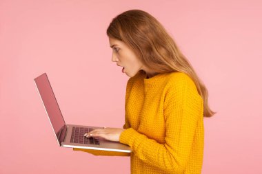 Süveterli, kucağında süveter tutan hayret dolu genç bir kızın yan görüntüsü.