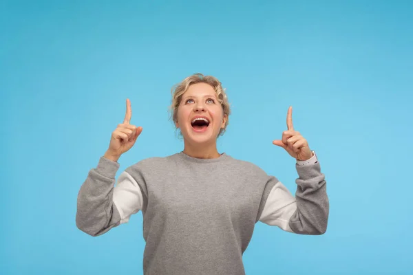 Wow, look up! Amazed woman with curly hair in sweatshirt pointin — 스톡 사진