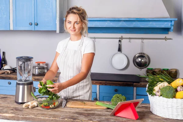 Attraktiv ung kvinna i förkläde matlagning grön sallad, förbereda v — Stockfoto