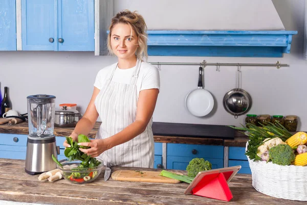 Attraktiv ung kvinne i forkle, grønn salat, klargjøring v – stockfoto