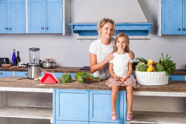 Beautiful mother in apron hugging daughter smiling at camera in — Stock Photo, Image