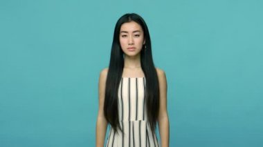 Evet, efendim! Uzun siyah saçlı ciddi sorumlu Asyalı kadın doğrudan kameraya bakıyor ve selam veriyor, komutayı dinliyor, emirlere itaat etmeye hazır. Mavi arka planda kapalı stüdyo çekimleri