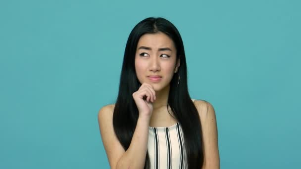 非常有吸引力和聪明的亚洲女人 有着一头长长的黑发 穿着讲究思想 有聪明的表情 有策略 有疑虑 室内拍摄 蓝色背景 — 图库视频影像