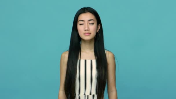 和平的亚洲女人 有着长长的黑发 穿着连衣裙 做着祈祷手势 闭着眼睛 练习专心 冥想和放松 在蓝色背景下隔离的工作室拍摄 — 图库视频影像