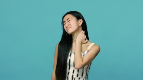 背中の首の痛みに苦しむ長いストレートの黒い髪を持つ疲労不健康なアジアの女性 筋肉をマッサージ 痛みを緩和するために 子宮頸椎のピンチ神経 スタジオショットは青の背景に隔離され — ストック動画