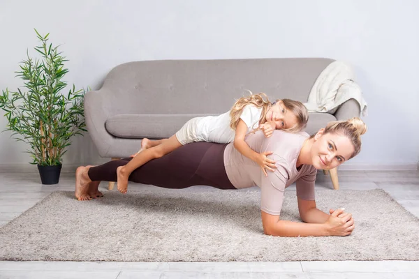 Veselý matka dělá prkno cvičení s malou dcerou na ní — Stock fotografie