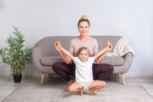 Beautiful young mother practicing yoga with little daughter, rai