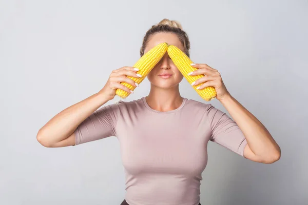 Portrait of positive woman covering eyes with corn cobs, fresh r — 스톡 사진