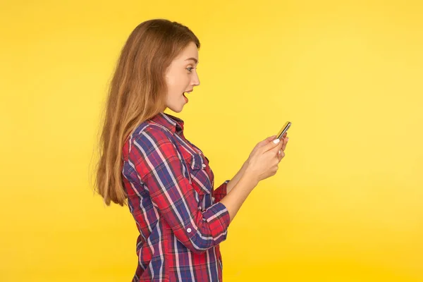 Side view of amazed ginger girl in casual shirt using cell phone — 스톡 사진