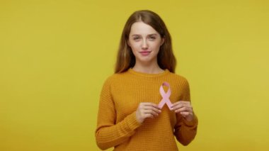 Elinde pembe kurdele, meme kanseri önleme işareti, hastalık bilinci ve sağlık sigortası olan sevimli, cana yakın, sevimli bir kız. Sarı arka planda izole edilmiş kapalı stüdyo çekimi