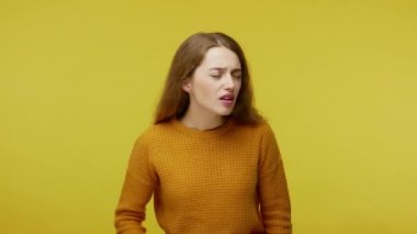 What? i don't listen! Annoyed girl holding arm near ear and pretending not to hear, showing bla bla hand gesture, uninterested in communication. indoor studio shot isolated on yellow background