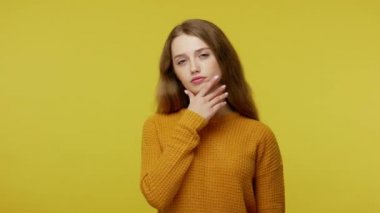 Thoughtful pretty girl with brown hair in pullover rubbing her chin and looking aside with pensive expression, pondering solution, doubting question. indoor studio shot isolated on yellow background