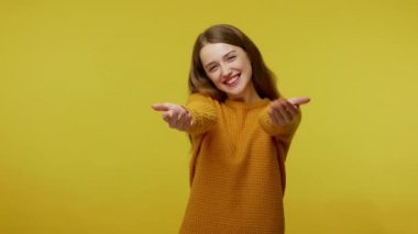 Come into my arms. Adorable happy girl with brown hair in pullover gesturing come here for free hugs and smiling sincerely with welcoming expression. indoor studio shot isolated on yellow background