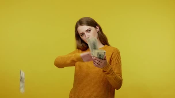 カジュアルな衣装を誇りに傲慢な女の子の周りにドル紙幣散乱し お金を投げ カメラで横柄な顔をし 大きな給料を誇る 黄色の背景に隔離された屋内スタジオで — ストック動画