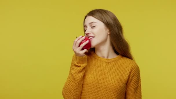 ベジタリアンライフスタイル ヘルスケア 積極的な空腹の美しい少女は赤いリンゴを食べて親指を表示し 笑顔で新鮮な食べ物 食事の栄養を楽しんでいます 黄色の背景に隔離された屋内スタジオで — ストック動画