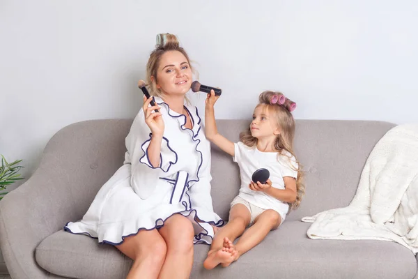 Feliz mamá y su hija con rulos en el pelo sentado en el sofá doin — Foto de Stock